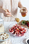 Frau süsst Erdbeeren und Rhabarber in Schüssel mit Honig