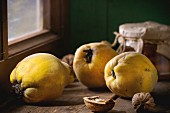 Three juicy quinces, walnuts and jar of honey over wooden table near window