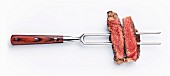 Slices of beef steak on meat fork on white background