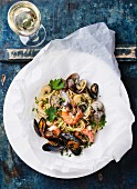 Seafood pasta and wine - Spaghetti with clams, prawns, sea scallops on blue background