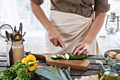 Woman cuts zucchini on wooden table near window
