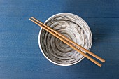Empty ceramic bowl with bamboo chopsticks over blue wooden surface