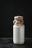 Glass bottle full of milk closed by paper and thread over black background
