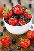 Erdbeeren und Heidelbeeren in Tasse auf Holztisch