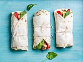 Tortilla wraps with grilled chicken fillet and fresh vegetables on blue painted wooden background