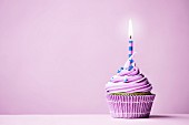 Lilafarbener Geburtstags-Cupcake mit brennender Kerze vor violettem Hintergrund