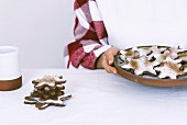 A woman is holding a plate full of snowflake cookies and a coffee cup and a pile of cookies accompanying her