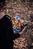 A woman holding a tray full of cinnamon rolls in the nature of dry leaves