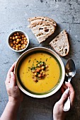 Female hands holding a bowl with pumpkin and roasted chickpea soup