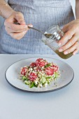 A woman is gettitng ready to drizzle a watermelon bulgur salad with lime and honey dressing