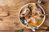 White ceramic plate with stewed rabbit with bouillon, salt and herbs, served with vintage cutlery over wooden background