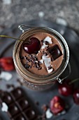 Chocolate coconut smoothie in a jar topped with cherry, dark chocolate, coconut flakes and cacao nibs