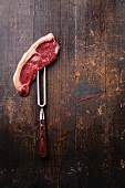 Rohes Striploin-Steak auf Fleischgabel vor Holzhintergrund