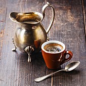 Tasse Espresso und silbernes Milchkännchen auf Holzuntergrund