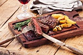 Medium rare grilled Beef steak Ribeye with roasted potato wedges on cutting board on dark wooden background