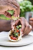 A man is squeezing lime on a slow cooked beef brisket chili taco while holding it with his other hand