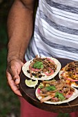 A man is getting ready to serve slow-cooked beef brisket tacos served on a wooden plate outdoors
