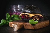 Black burger with stews, cheese, red cabbage and balsamic sauce served on wooden chopping board with fresh basil