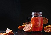Sliced Sicilian Blood oranges and glass mason jar of fresh red orange juice over old wooden table
