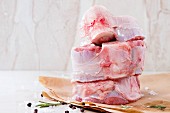 Stack of raw osso buco meat on crumpled paper with salt, pepper and rosemary over white marble as background