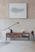 Black table lamp on simple low sideboard made from reclaimed wood below framed artwork