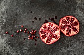 Two halves of a pomegranate and seeds and juice on a grey metal surface