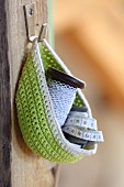 Green crocheted basket hung from hook on wooden board