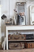 Old suitcases on shelves below console table decorated with vintage ornaments and jug of proteas