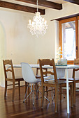 Dining table, rustic wooden chairs and white classic chairs below chandelier