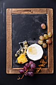Cheese with honey, nuts and grapes on vintage slate chalk board