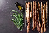 Fresh baked homemade grissini bread sticks in vintage metal grid box with olive oil and herbs rosemary and thym