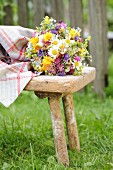 Vase of colourful wildflowers on vintage wooden stool in garden