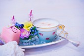 Cup of cappuccino, flower arrangement and petit four