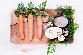 Carrots, carrot leaves, feathers and various decorated eggs in wooden dish
