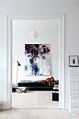 Couch below abstract painting seen through doorway