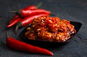 Black plastic dish with chilli paste in olive oil with fresh whole birds-eye chillies