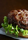 Grilled beef burger on a white bun with curly lettuce, lying on white wax paper