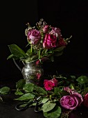 Silver jug of roses against black background