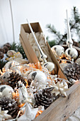 Silver Christmas tree baubles, pine cones and fairy lights in wooden crate