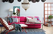 Pinkfarbene Couch mit verschiedenen Kissen vor hellgrauer Wandverkleidung und Wanddekoration mit Hüten