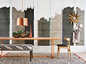 Filigranes, orangefarbenes Metall-Tischgestell vor Wandgestaltung im Ethno-Stil