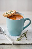 Tomato soup in a blue mug with creme cheese baguette and thyme