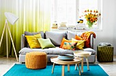 Farbenfrohes Wohnzimmer mit türkisblauem Teppich, grauer Polstercouch und gelben, orangefarbenen Kissen