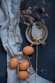 Easter decorations with chicken eggs and a branch beside a chicken motif on a blue background