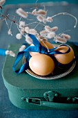 Eggs and blue satin ribbon on pewter plate on top of miniature suitcase