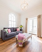 A reduced living area with an upholstered table and couch in front of round arched windows