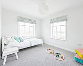 Weisses Bett und buntes Holzspielzeug auf grauem Teppichboden