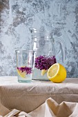 Glass and pitcher of lilac lemonade water with lemon and lilac flowers
