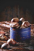 Purple Tin jar with raw edible chestnuts over wooden table