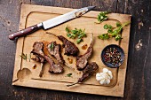 Roasted lamb ribs and kitchen knife on wooden cutting board on dark background